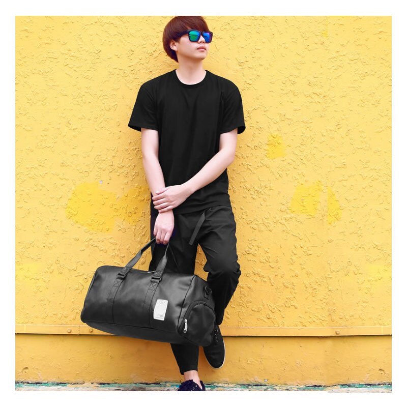 Person in black attire against yellow wall holding a waterproof sports gym bag.
